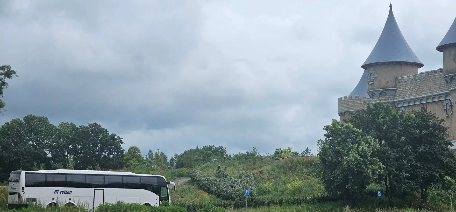 Touringcar van RT Reizen langs de weg in de Achterhoek, met de torens van een kasteel boven de bomen.