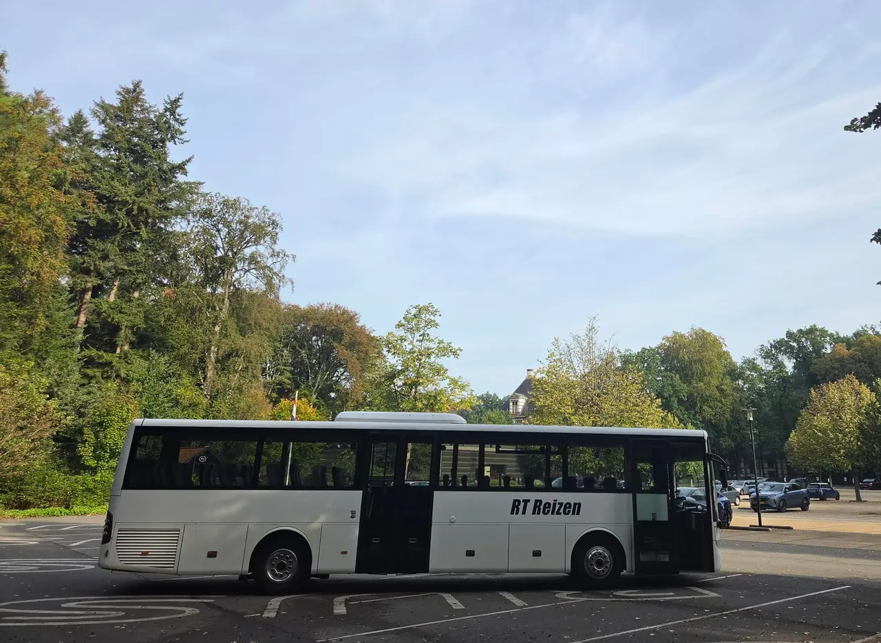 Bus van RT Reizen met open deuren op een parkeerplaats tussen de bomen in Apeldoorn.