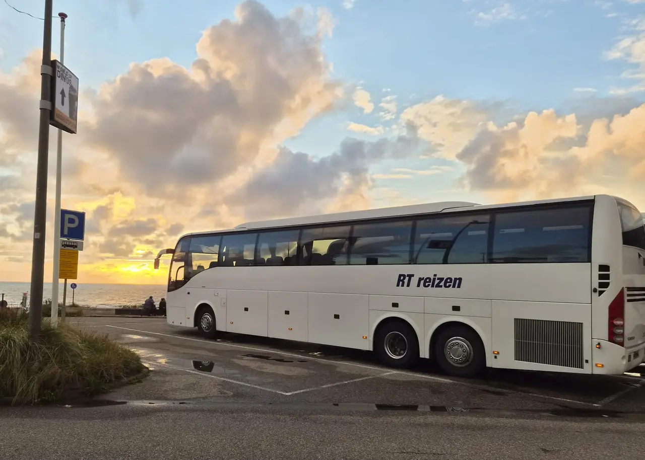 Bus van RT Reizen op een parkeerplaats aan zee, bij zonsondergang.