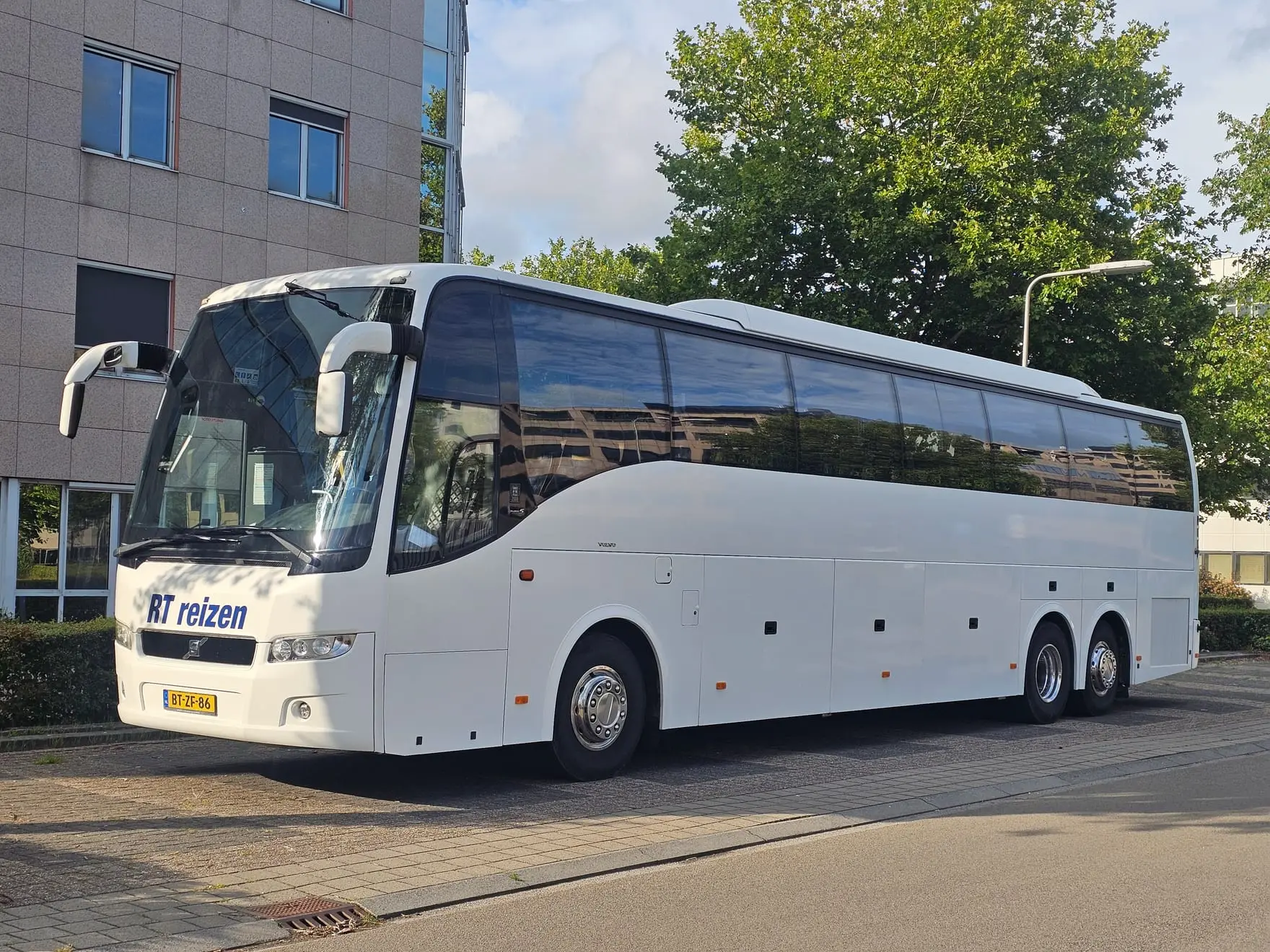 Touringcar van RT Reizen langs een gebouw in de late middagzon