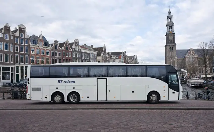 Touringcar van RT Reizen aan een Amsterdamse gracht, met de Westertoren op de achtergrond.