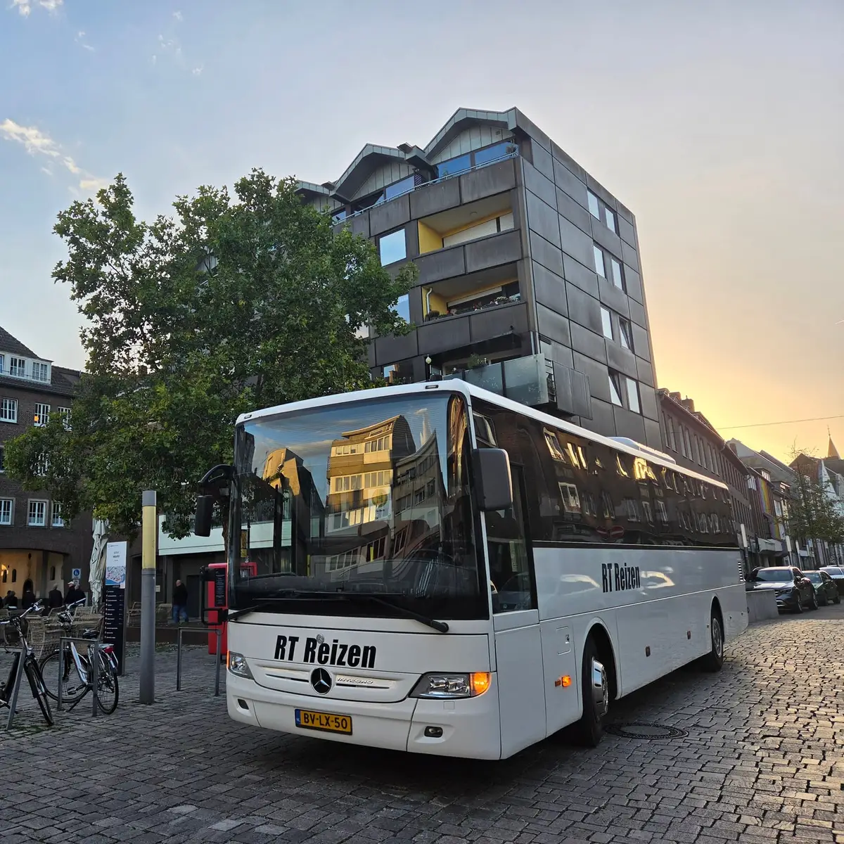 Der Reisebus von RT Reizen auf dem Kopfsteinpflaster am Alten Markt in Emmerich, dahinter ein Wohnhaus im Abendlicht.