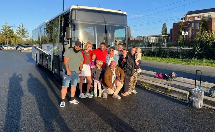 Een gezelschap met kinderen staat lachend voor de bus van RT Reizen.