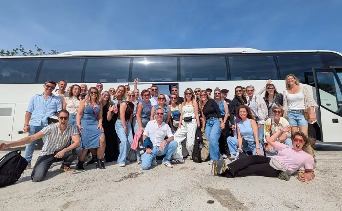 Een groep gasten staat lachend voor de touringcar van RT Reizen.