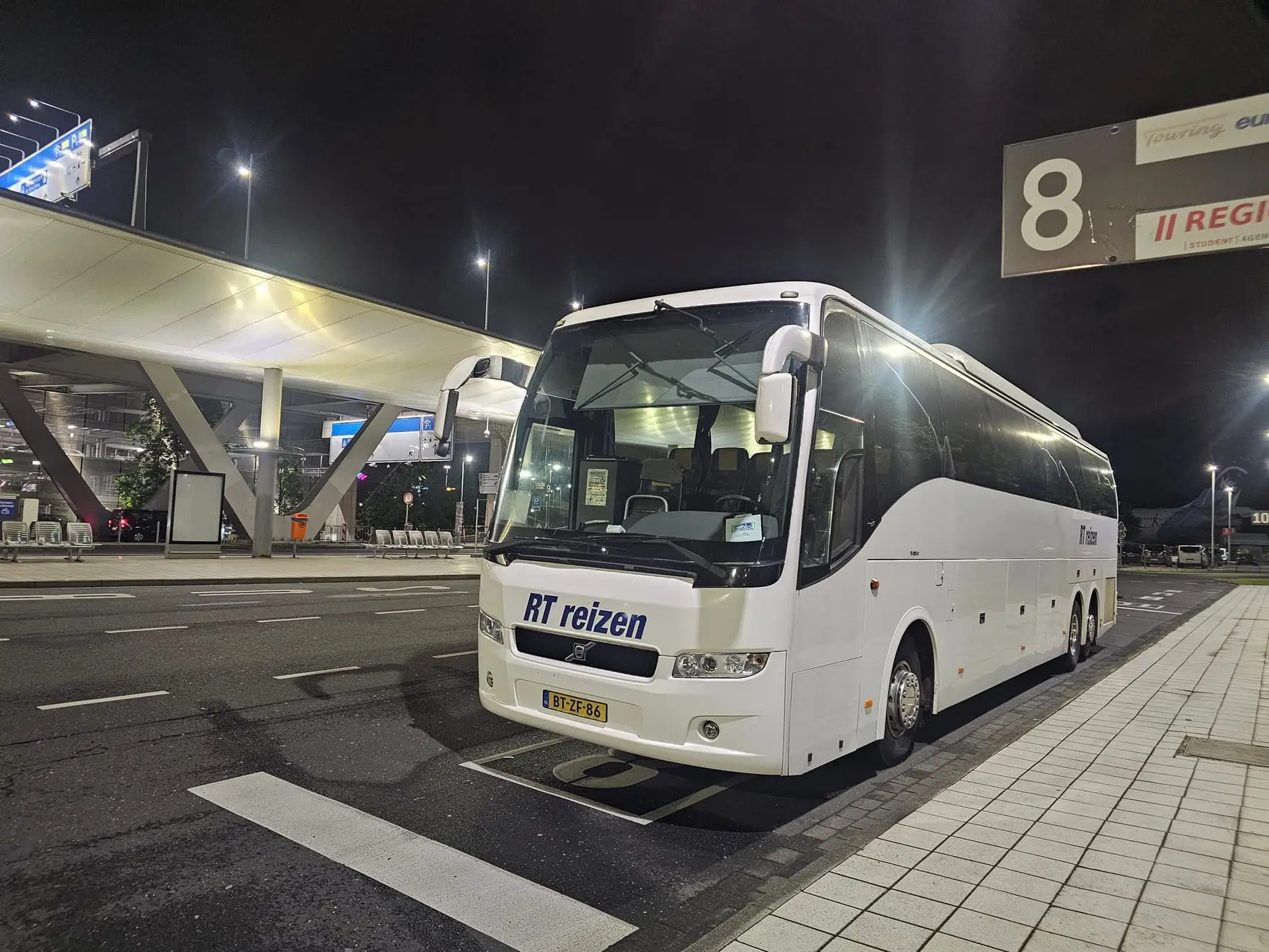 De touringcar van RT Reizen staat 's nachts bij de vertrekhal van de luchthaven.