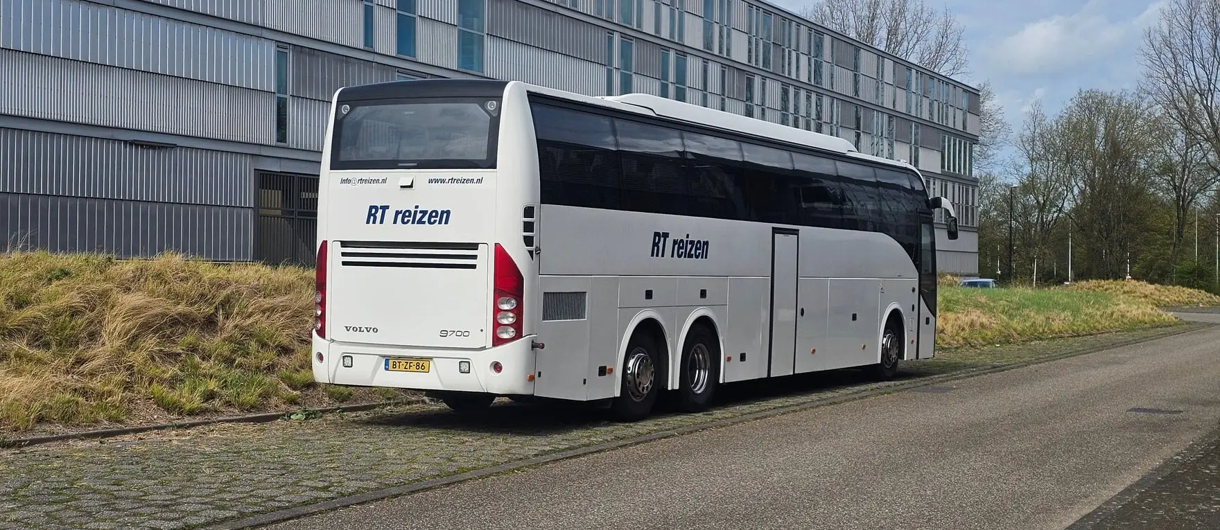 Touringcar van RT Reizen langs de weg bij een bedrijfspand, van achteren gezien.