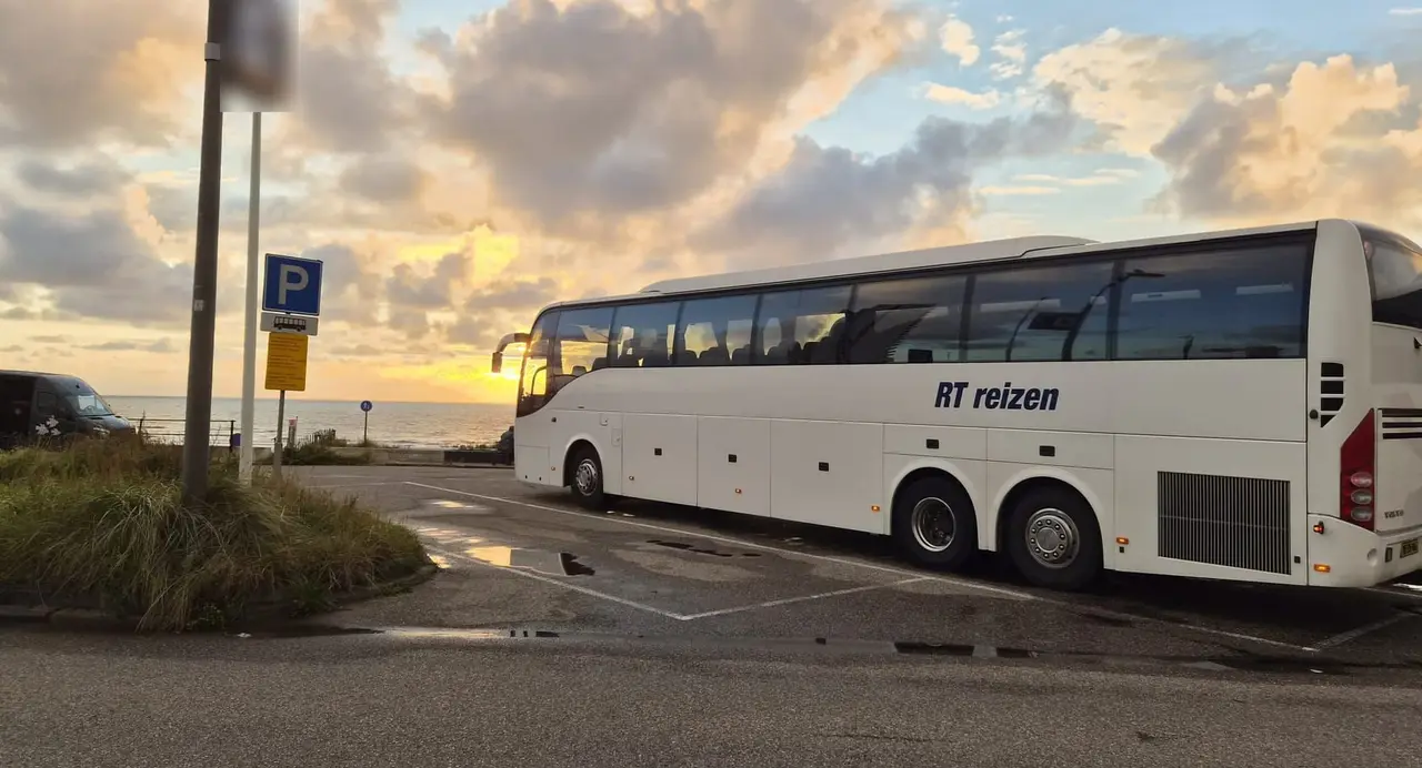 Touringcar van RT Reizen op een parkeerplaats aan zee bij zonsondergang.