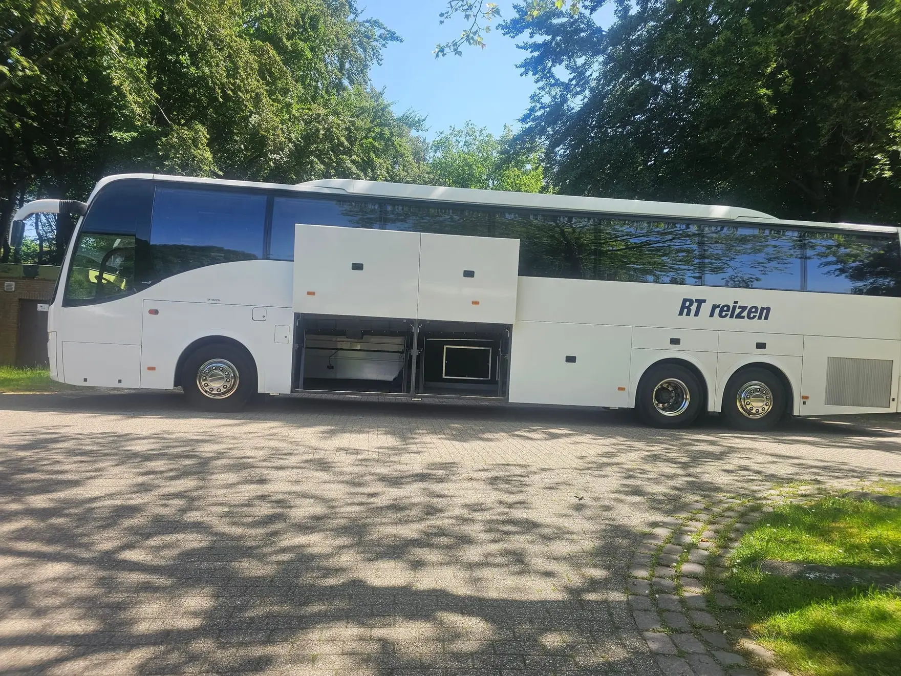 Touringcar van RT Reizen van opzij met het bagageruim open, klaar voor vertrek.