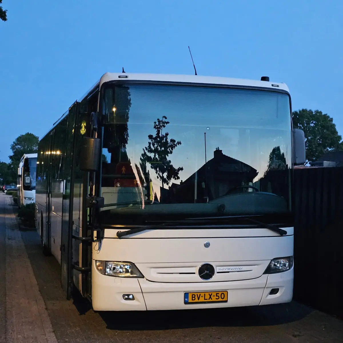 Bus van RT Reizen langs de weg in de schemering, met een tweede bus erachter.
