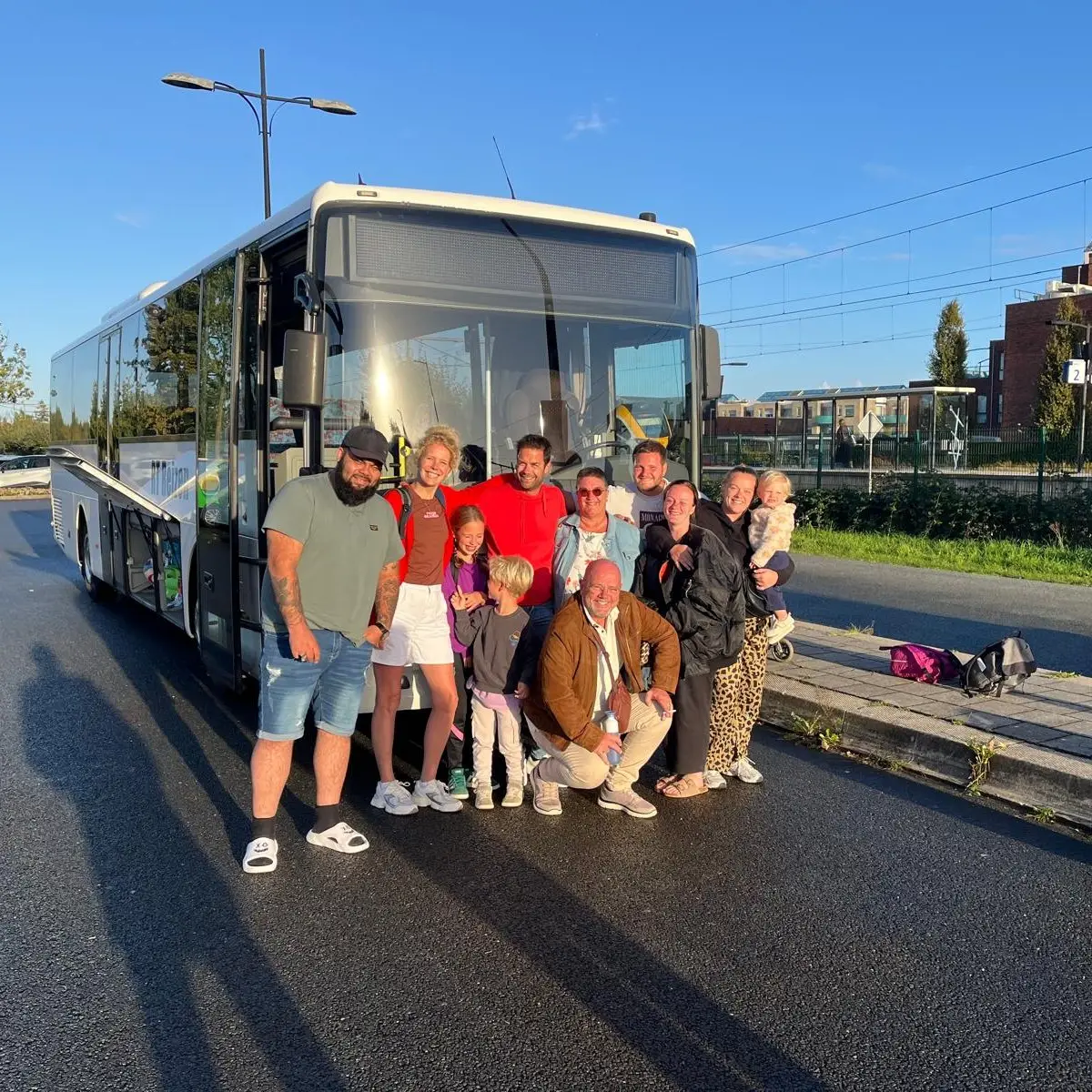 Een gezelschap met kinderen voor de bus van RT Reizen, met de bagage ernaast.