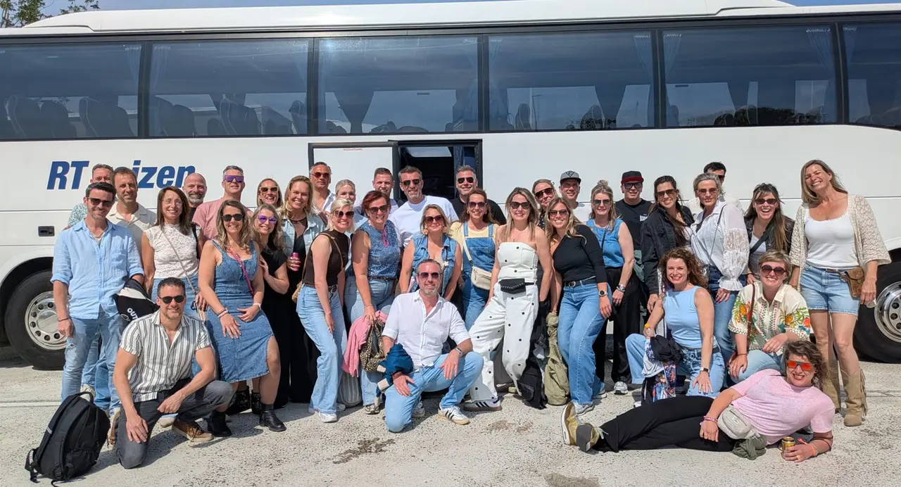 Een grote groep staat lachend voor de touringcar van RT Reizen.